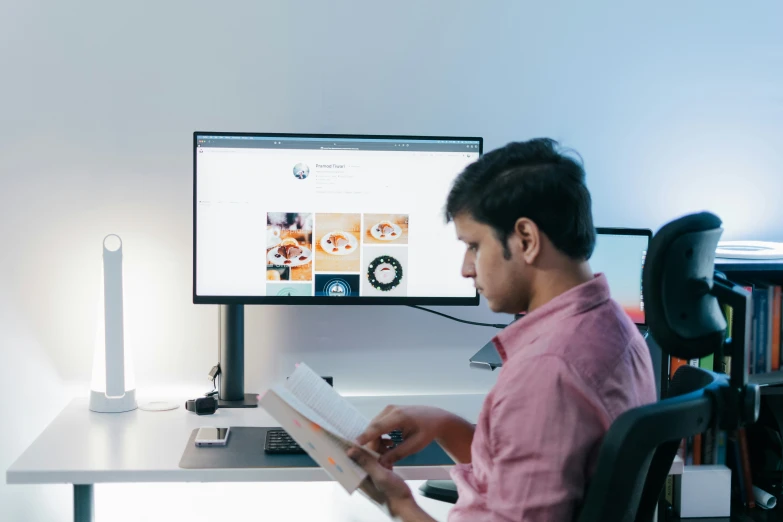 a man reading a book while looking at the monitor