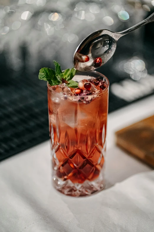 a spoon taking up a cherry drink out of a tall glass