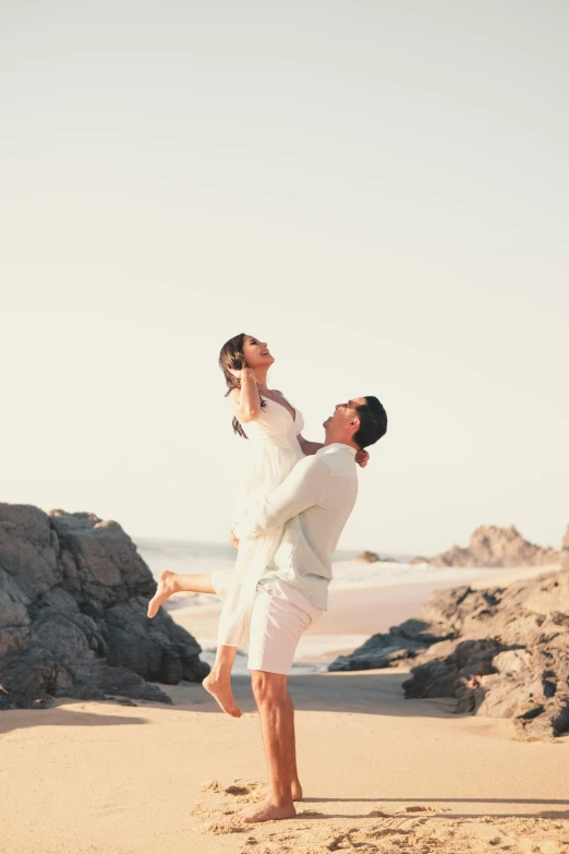 two people standing on the beach with one holding a woman