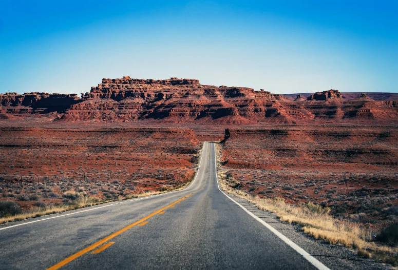 an empty road with yellow line at the center, surrounded by a tall red cliff in the distance