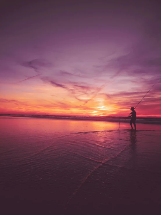 a man is fishing in the ocean as the sun sets