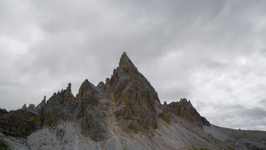 a very tall, gray rock mountain with little clouds above