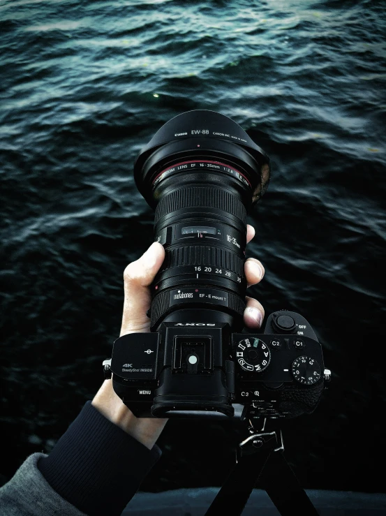 person holding camera near body of water at night