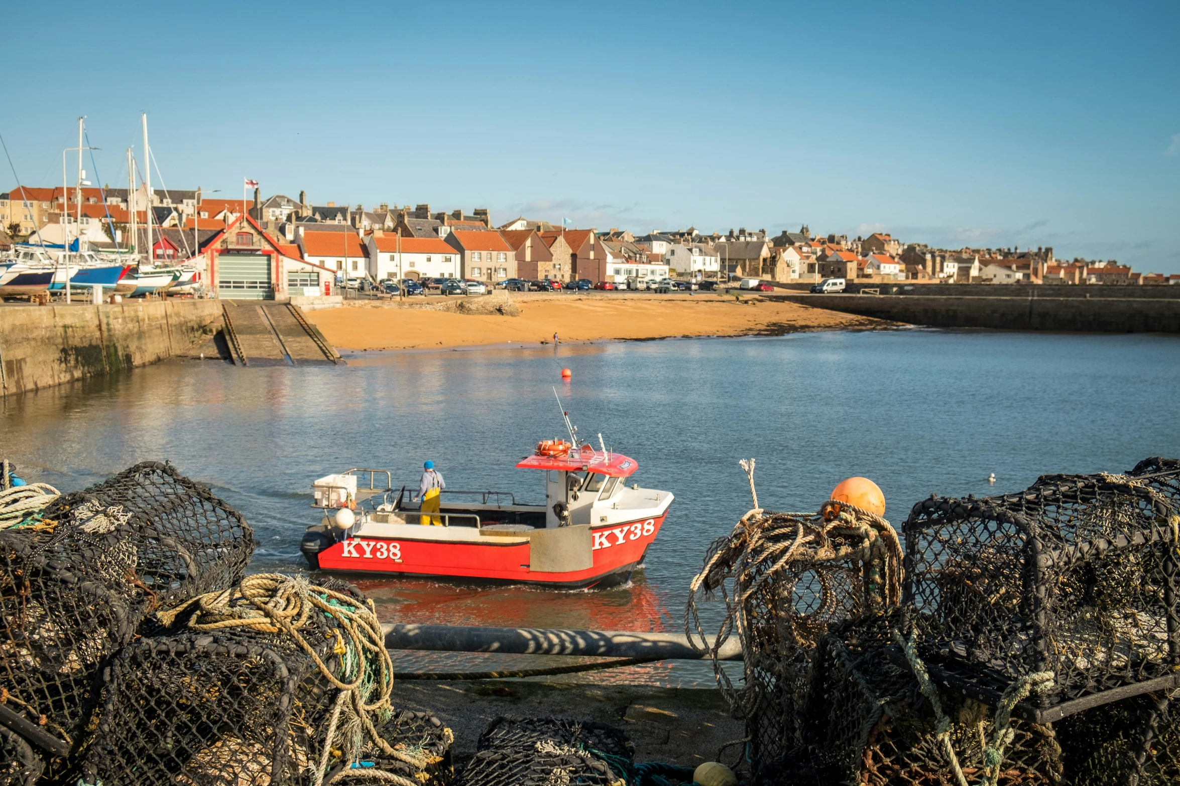 a small boat parked on the beach surrounded by metal lobster nets