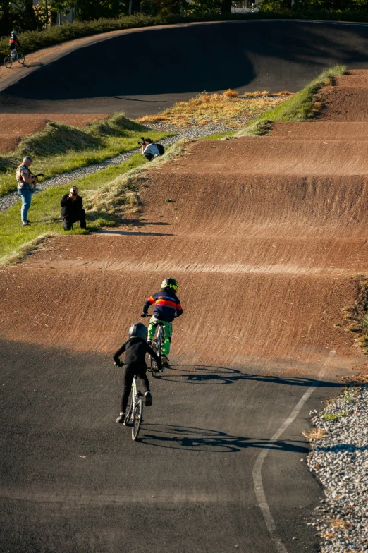 three people on bicycles, one has a black jacket and the other is red and green