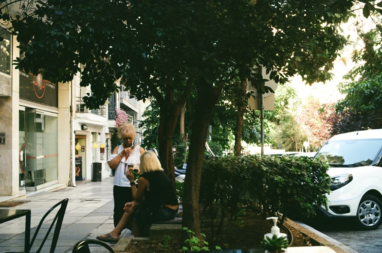 two women are talking on a phone at the sidewalk