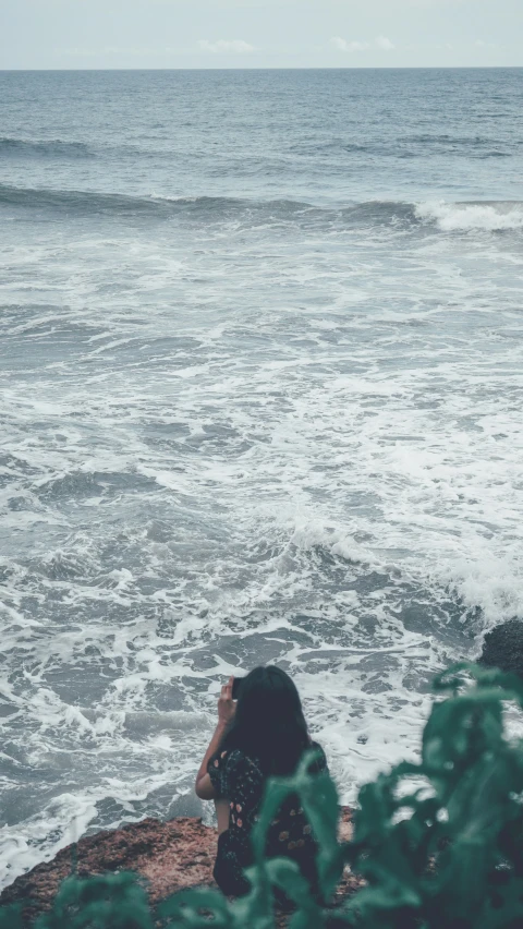 a person sits on rocks in front of the ocean