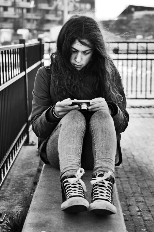 a young lady looking at her phone while sitting on a bench