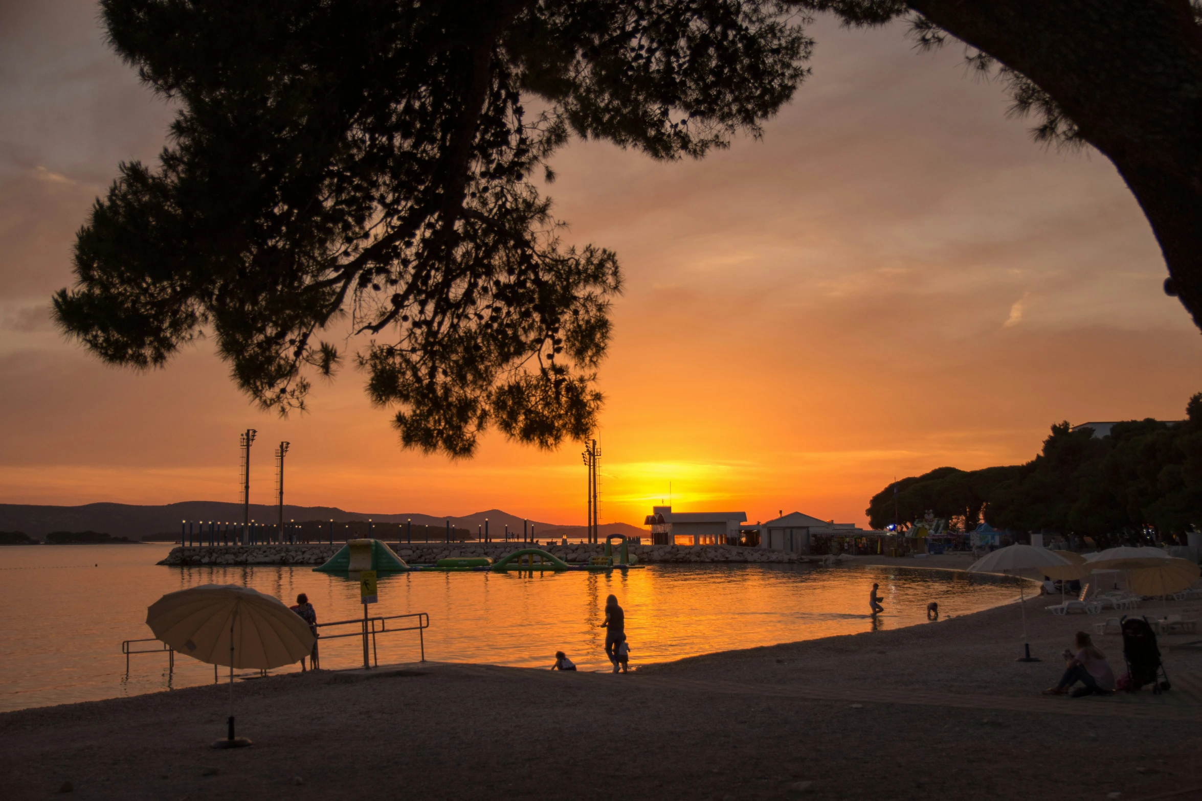 people are sitting by the water as a sunset is seen