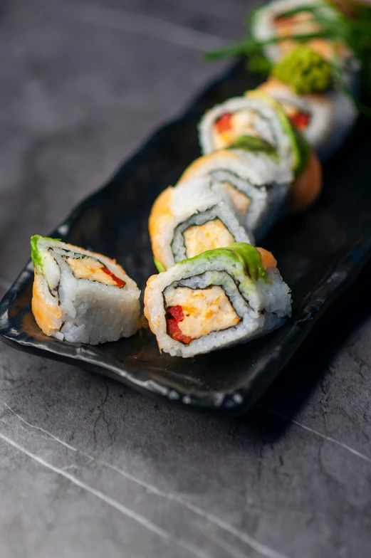 sushi rolls sit on a black plate with cucumber