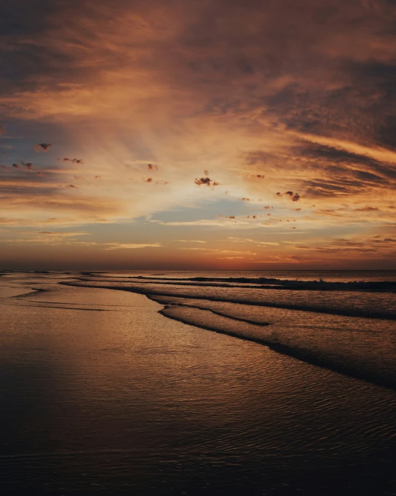 the sun sets at a beautiful beach with some waves coming in