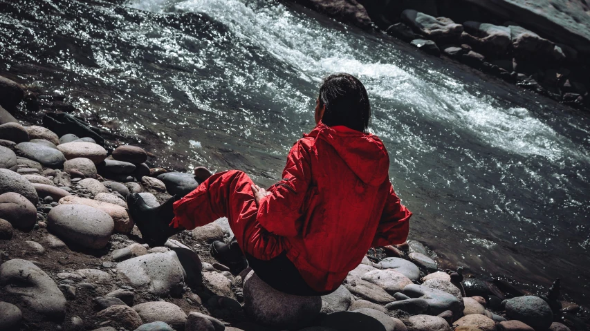 the person sitting in a red jacket looks at water