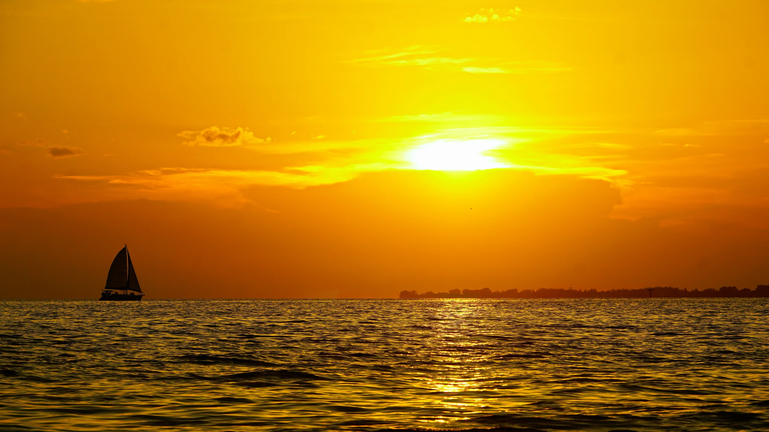 a sail boat with the sun setting on the horizon