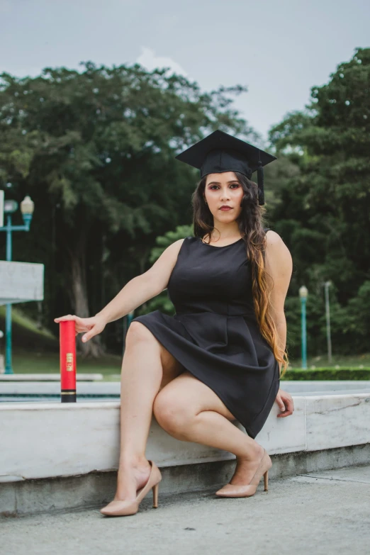 young woman sitting down for graduation in a short black dress