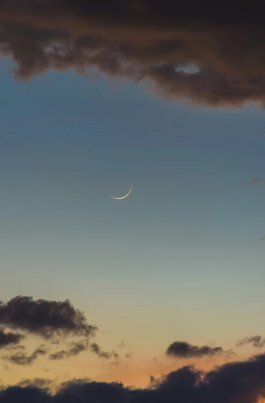 the crescent moon in the sky, as seen from below clouds