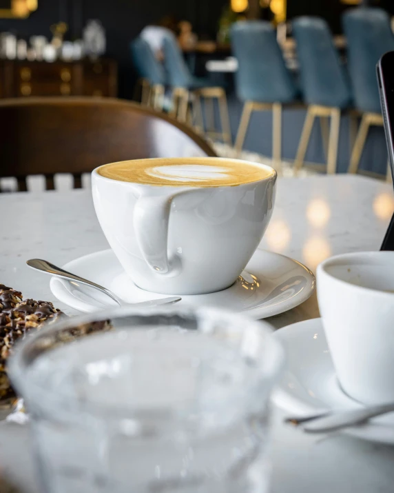 two cups of coffee on plates next to a cellphone