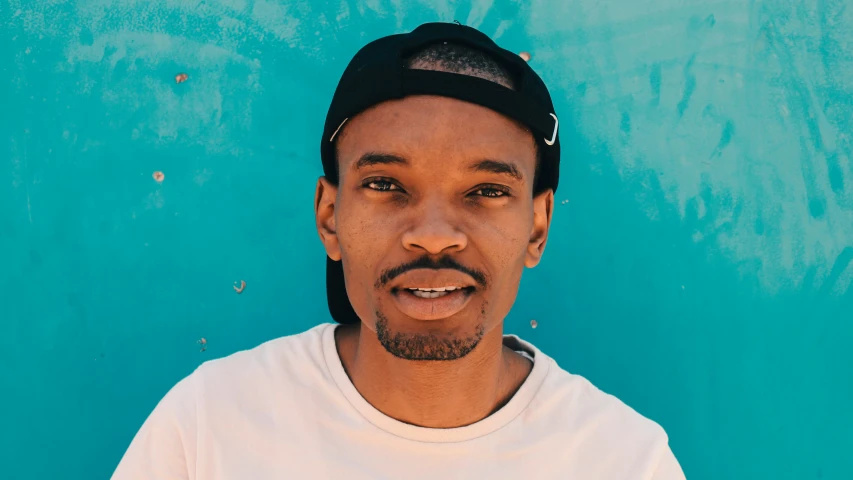 a young man in a hat smiling in front of a blue wall