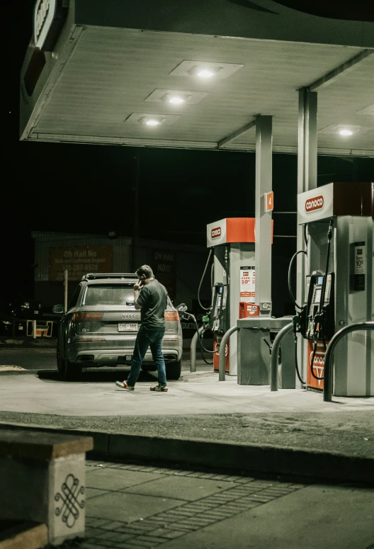 there is a man that is walking next to the gas pumps