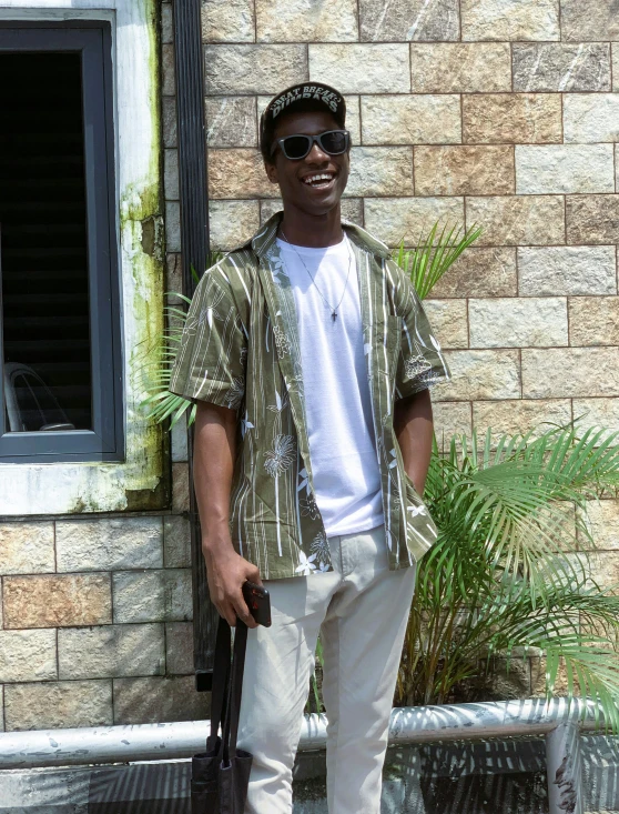 man wearing sunglasses and a striped jacket standing against a brick wall