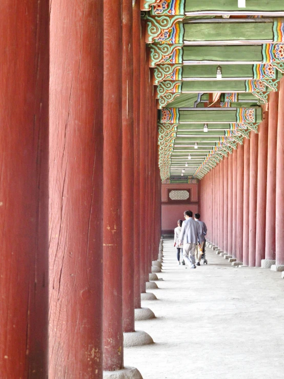 people walking down a walkway near large red columns