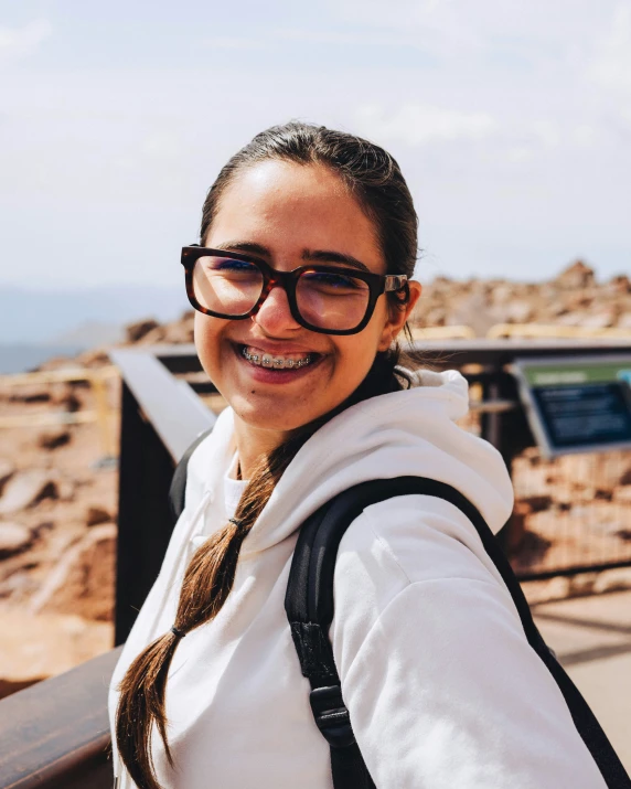a smiling woman with a backpack and black rimmed glasses