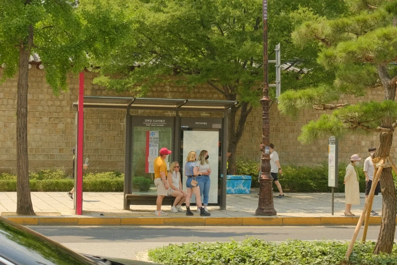 several people standing outside of a bus stop next to trees