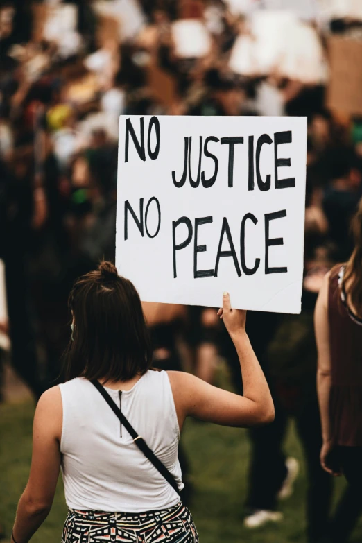 a woman holds up a sign that reads no justice and no peace