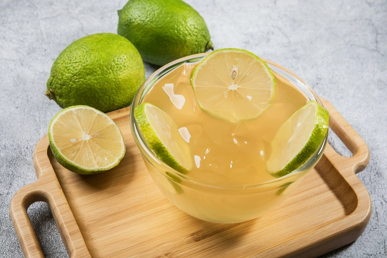 a clear pitcher of alcohol sitting on a wooden  board with limes