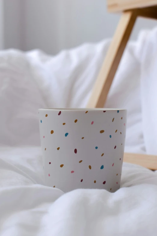 a white cup with tiny sprinkles sits on a white bed