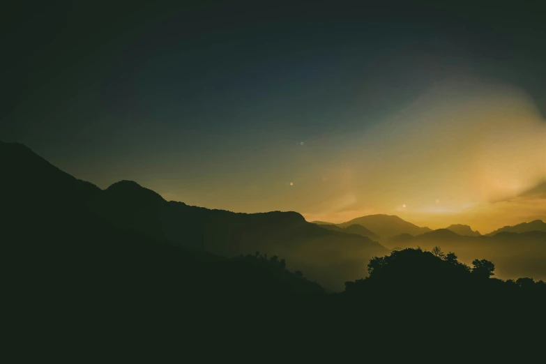 the sun is rising over the mountains with some trees on it