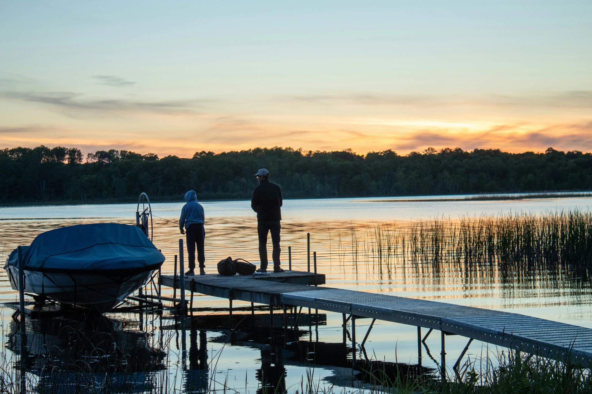 two people standing at the end of a dock near a boat