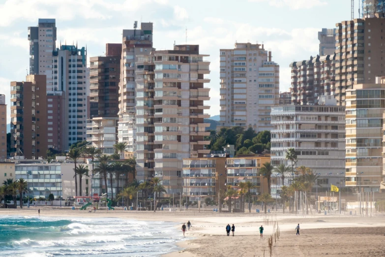 several people walking on a beach in front of a bunch of buildings