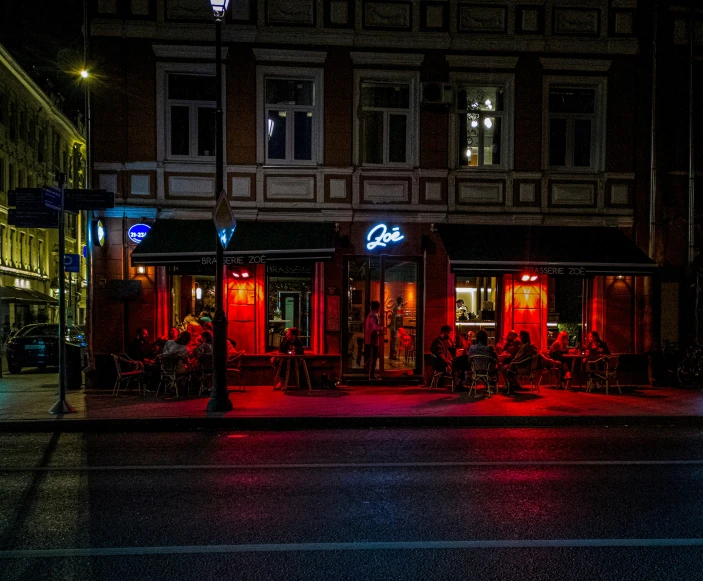 a dark street with a store front and people sitting on a bench in the dark