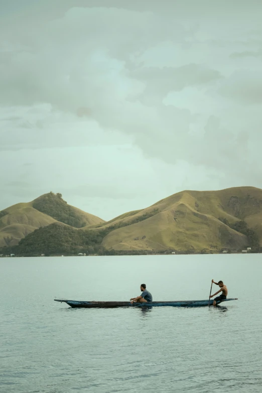 two people on a boat on water with mountains in background