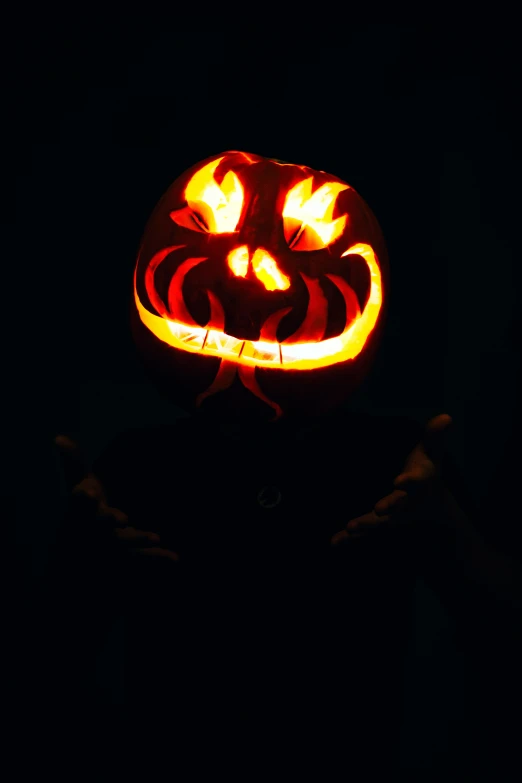 a person is holding a carved pumpkin lit up at night