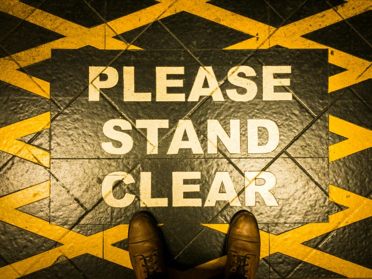 feet on a tiled floor with a sign stating please stand clear