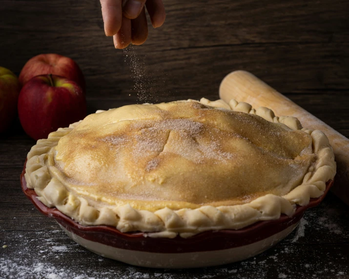 someone sprinkling flour on some apple pie