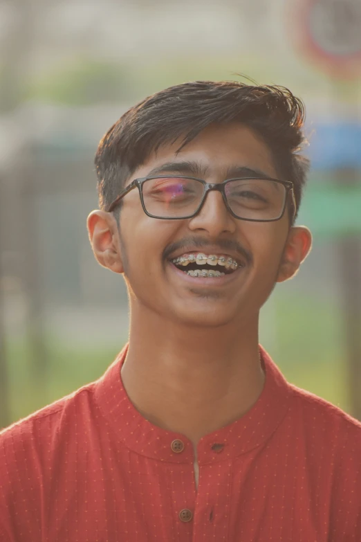 a man with glasses smiles in front of a building