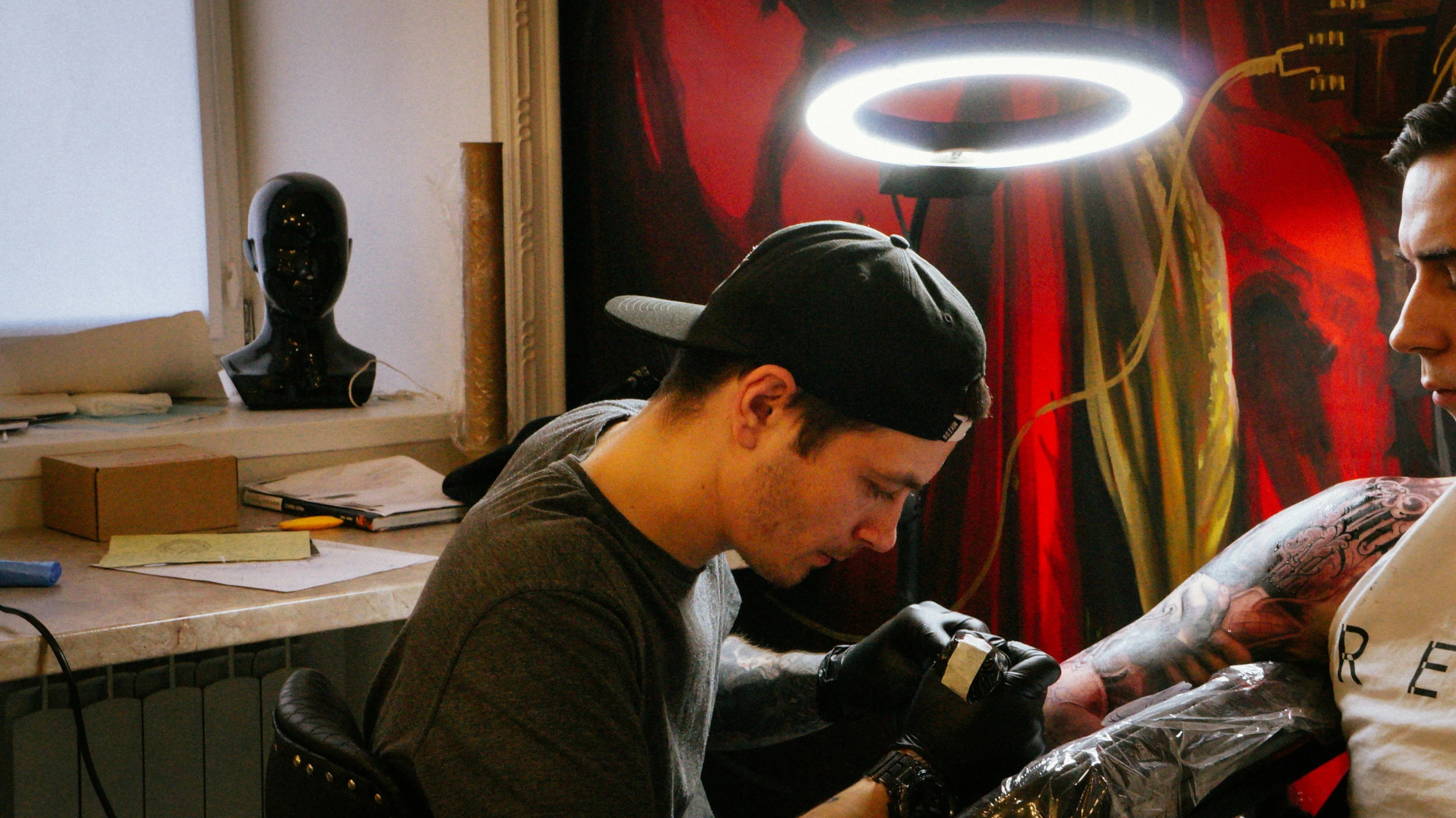 a man getting a tattoo while another mans looks on