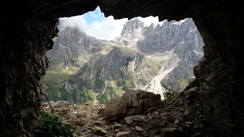 a rocky and cloudy mountainside are seen through a cave