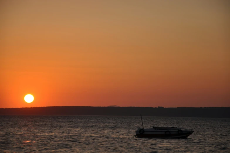 a boat is sitting in the water in front of a sunset