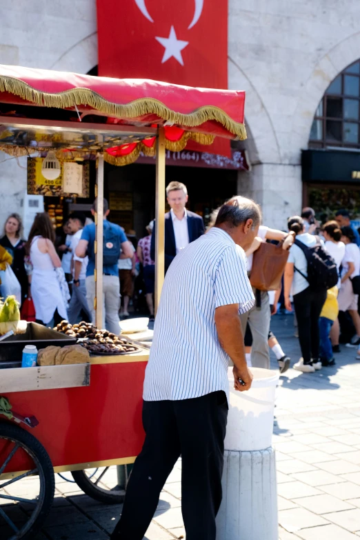 an older man hing his cart past a stand selling fresh fruit