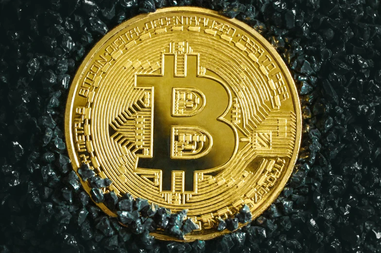 a golden bitcoin laying on a black surface