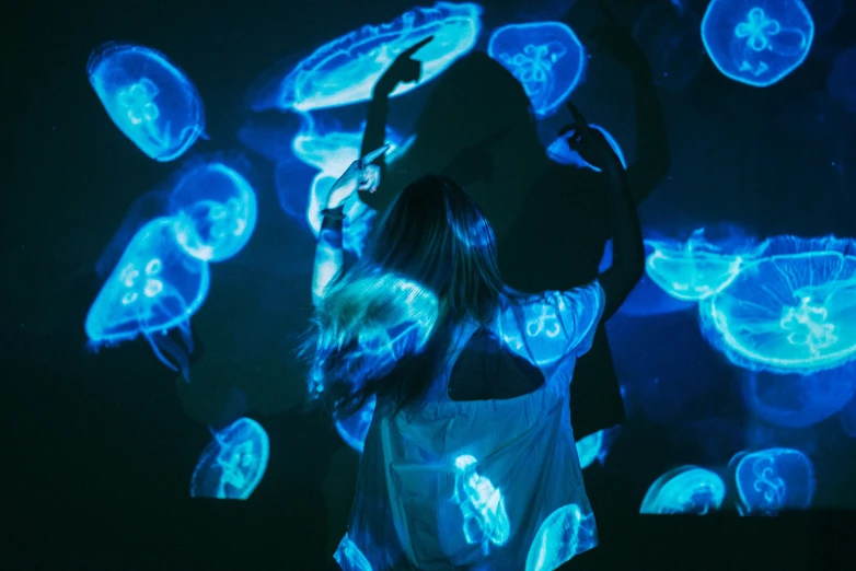 a woman dancing with bright lights in front of an array of jellyfish