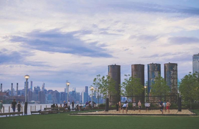 people walk on the grass in front of large silos