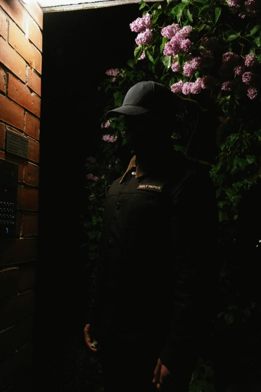 a black person standing with flowers behind a brick wall