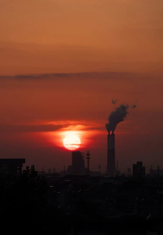 smoke stacks coming out of a factory tower with the sun setting behind it