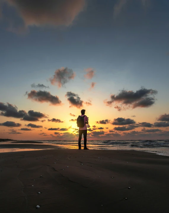 a person standing on a beach near the ocean at sunset