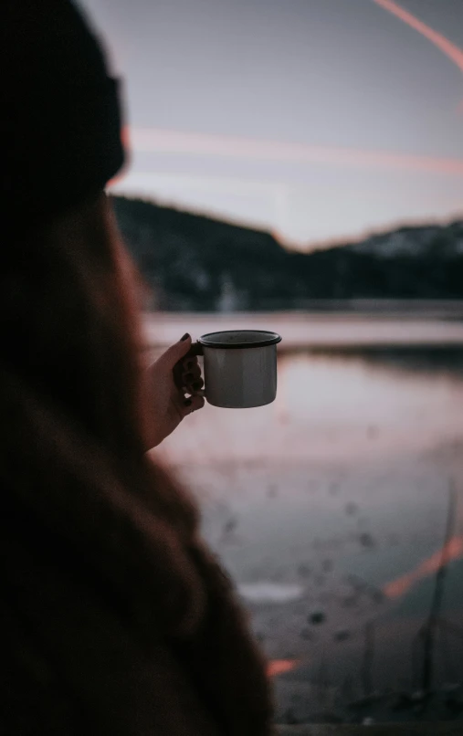 a woman holding a paper cup with the reflection of a mountain in it