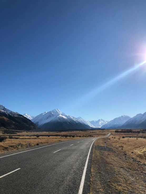 the sun shining down on the mountains and a deserted road